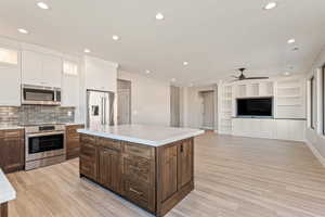 Two tone kitchen featuring stainless steel appliances, open floor plan, recessed lighting, light wood-type flooring, and built in features
