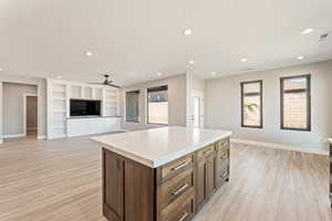 Kitchen with open floor plan, light countertops, a center island, a textured ceiling, and light wood finished floors