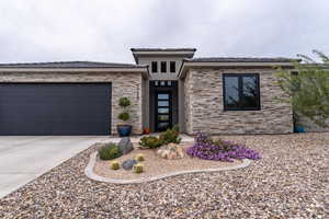 Prairie-style home featuring driveway, a garage, stone siding, and stucco siding