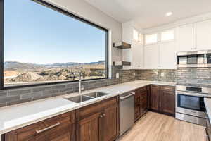 Kitchen with stainless steel appliances, glass insert cabinets, two tone cabinets, light wood-type flooring, and decorative backsplash