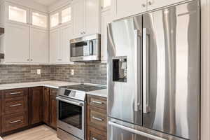 Two tone kitchen with stainless steel appliances, glass fronted cabinets, dual tone cabinetry, backsplash, and light wood-style floors