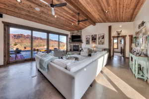 Living room with a ceiling fan, concrete flooring, a high wood beamed ceiling, recessed lighting, and floor to ceiling stone fireplace