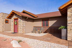 Doorway to property featuring stone siding, stucco siding, a metal roof, and a patio area