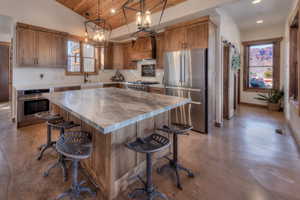Kitchen with stainless steel appliances, concrete flooring, Knotty Alder cabinetry, Leathered Quartzite island, and a breakfast bar