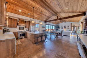 Open floor plan with kitchen island, wet bar and desk area, stainless steel appliances, and a high wooden beamed ceiling
