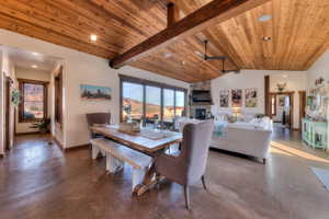 Dining room featuring concrete flooring, a ceiling fan, a stone fireplace, a high wood beamed ceiling, and recessed lighting