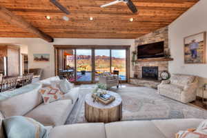 Living room with sliding glass doors to outdoor living space, a vaulted wood ceiling, and floor to ceiling stone fireplace