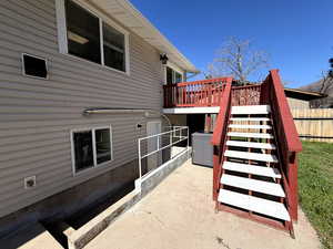 View of side of home with a wooden deck and a patio featuring white vinyl decking and redwood railing and trim.