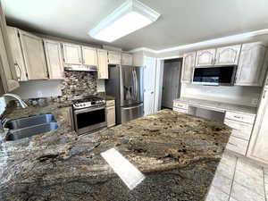 Kitchen featuring stainless steel appliances, decorative backsplash, light tile patterned floors, a peninsula, and dark stone counters