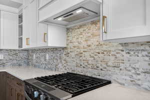 Kitchen featuring extractor fan, decorative backsplash, two tone cabinetry, light stone countertops, and open shelves