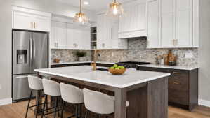 Gourmet kitchen featuring a central island with countertop seating, two-tone cabinetry, a mosaic tile backsplash, stainless steel appliances, and pendant lighting
