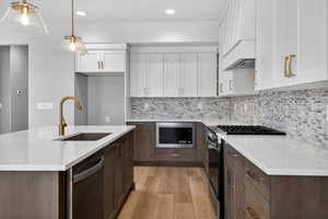 Kitchen with a kitchen island with sink, stainless steel appliances, light stone counters, two tone cabinets, and light wood finished floors