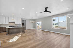 Unfurnished living room with hanging lights, a ceiling fan, and light wood-style floors