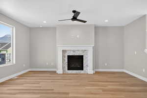 Unfurnished living room with light wood-type flooring, a ceiling fan, a fireplace, and recessed lighting
