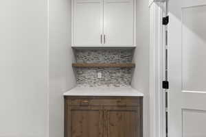 Bar area with backsplash, light stone counters, and open shelves