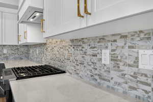 Kitchen with white cabinets, range with gas stovetop, light stone countertops, and backsplash