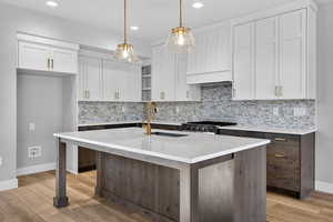 Dual tone kitchen featuring two tone color scheme, tasteful backsplash, a center island with sink, pendant lighting, and light stone counters