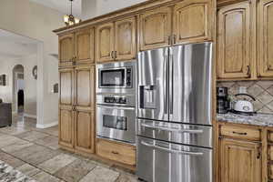 Kitchen featuring stainless steel appliances, arched walkways, decorative backsplash, light stone countertops, and wood finish cabinets