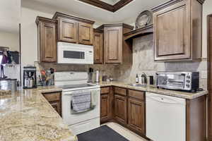 Kitchen featuring white appliances, light stone counters, wood finish cabinetry, and tasteful backsplash