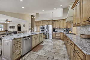 Kitchen featuring a kitchen island with sink, stainless steel appliances, light stone countertops, ceiling fan, and backsplash
