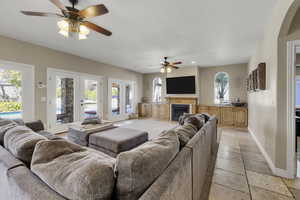 Living room featuring french doors, a ceiling fan, a glass covered fireplace, and arched walkways