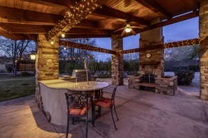 Patio terrace at dusk featuring exterior kitchen, an outdoor stone fireplace, a patio, and a ceiling fan