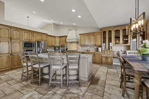 Kitchen featuring vaulted ceiling, a kitchen island with sink, a kitchen breakfast bar, glass fronted cabinets, and stainless steel appliances