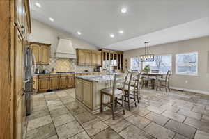 Kitchen featuring a breakfast bar, lofted ceiling, light stone counters, a center island with sink, and stainless steel appliances