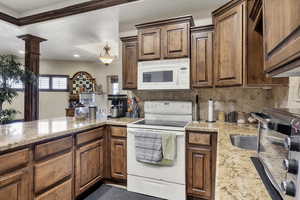 Kitchen featuring white appliances, light stone countertops, wood finish cabinets, and decorative backsplash