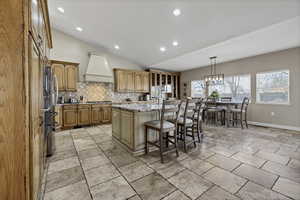 Kitchen featuring a breakfast bar area, vaulted ceiling, a kitchen island, light stone countertops, and glass fronted cabinets