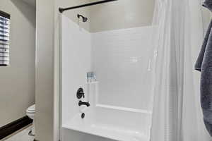 Bathroom featuring toilet and shower / bath combination with curtain