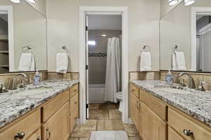 Full bathroom with two vanities, stone tile floors, and shower / tub combo with curtain