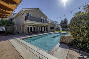 Outdoor pool with a patio, french doors, and a balcony