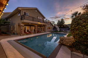 Back of house featuring a patio, an outdoor pool, stucco siding, and stone siding