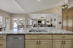 Kitchen featuring open floor plan, light wood finish cabinets, stainless steel dishwasher, a ceiling fan, and lofted ceiling
