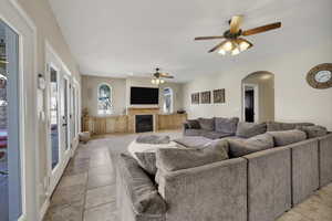Living area featuring ceiling fan, arched walkways, and a glass covered fireplace