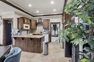 Kitchen featuring a kitchen breakfast bar, light stone countertops, backsplash, white appliances, and a peninsula