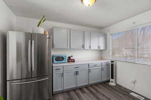 Kitchen featuring freestanding refrigerator, light countertops, gray cabinets, and dark wood-style floors