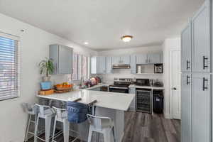 Kitchen with gray cabinetry, a kitchen bar, wine cooler, a peninsula, and stainless steel electric range oven