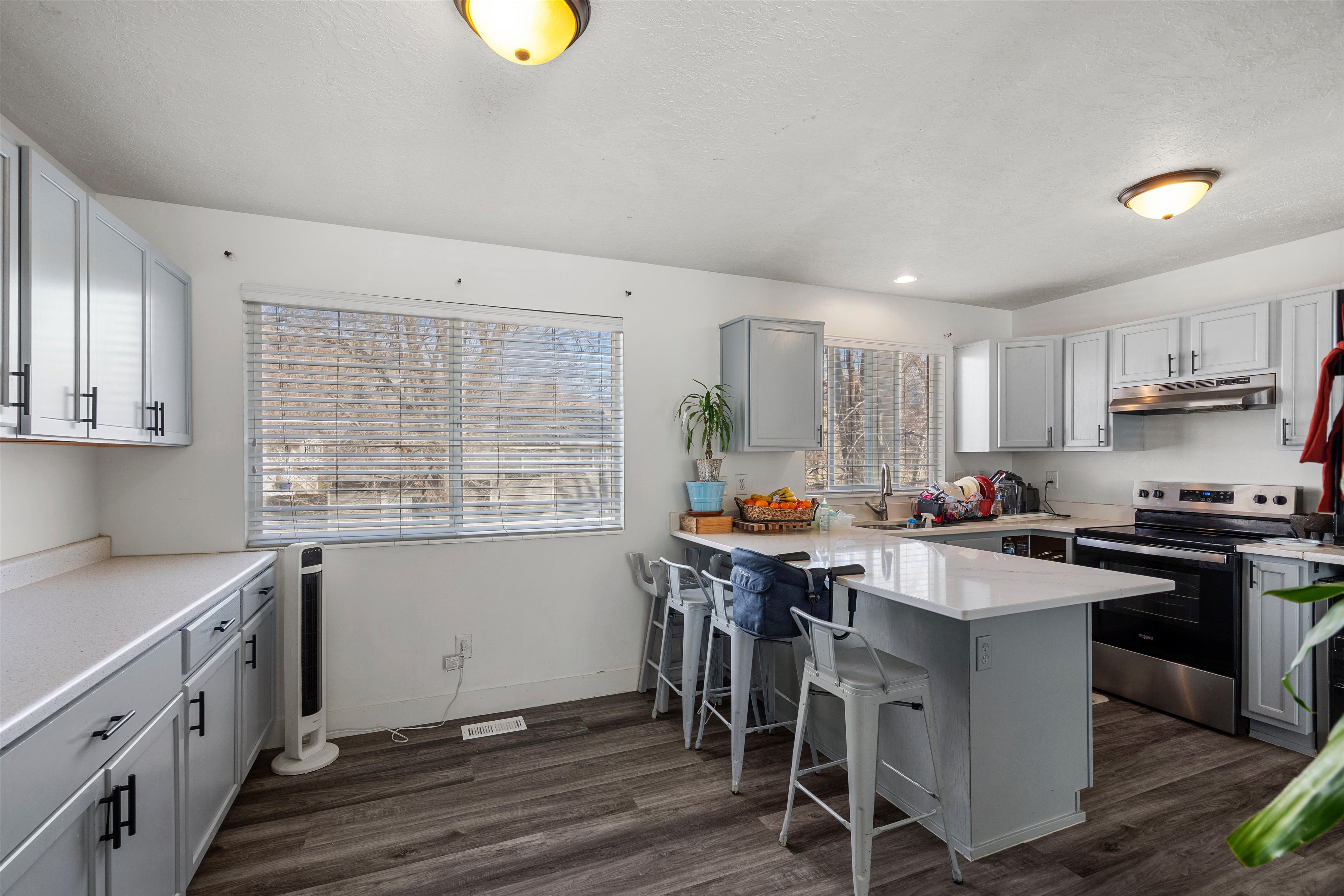 Kitchen featuring stainless steel range with electric stovetop, a breakfast bar, a peninsula, dark wood-style flooring, and gray cabinets