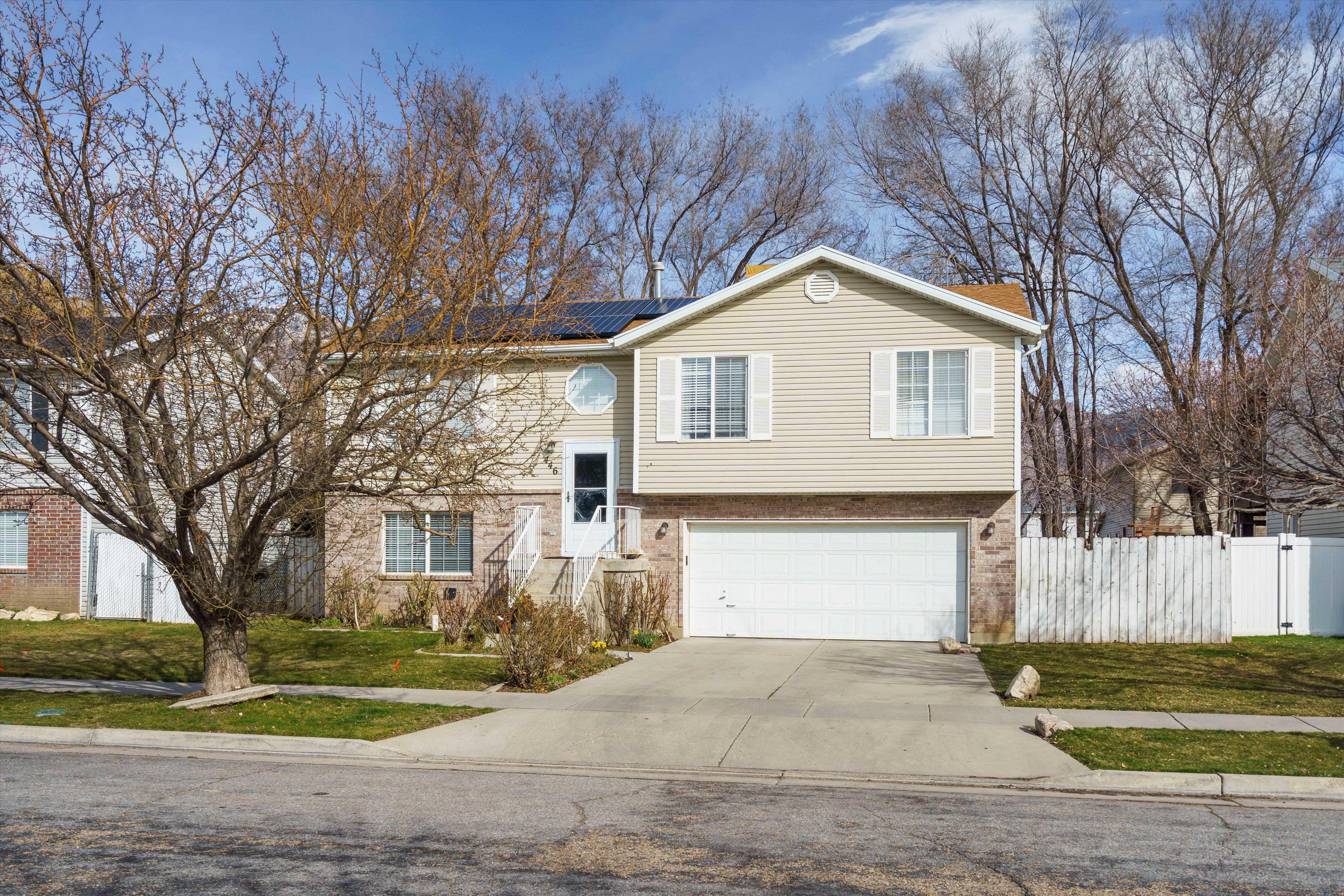 Raised ranch featuring solar panels, driveway, and a garage