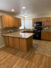 Kitchen with a peninsula, black appliances, light wood-type flooring, wood finish cabinets, and decorative backsplash