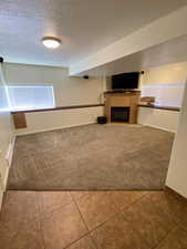 Unfurnished Family room featuring a textured ceiling, a fireplace, tile patterned floors, and carpet