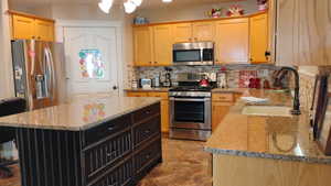 Dual tone kitchen featuring stainless steel appliances, a kitchen island, light stone counters, decorative backsplash, and two tone cabinets