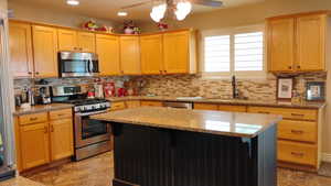 Kitchen with stainless steel appliances, a center island, ceiling fan, light stone counters, and recessed lighting
