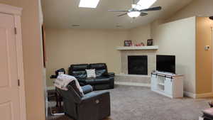 Carpeted living area featuring a ceiling fan, a fireplace, and lofted ceiling