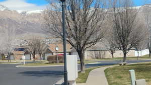 View of asphalt road with street lights, sidewalks, a mountain view, a residential view, and curbs