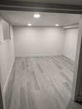 Finished below grade area with light wood-style flooring, recessed lighting, and a textured ceiling