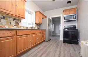 Kitchen featuring stainless steel appliances, light countertops, radiator heating unit, light wood-type flooring, and decorative backsplash