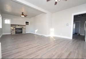 Unfurnished living room featuring a ceiling fan, wood finished floors, and a fireplace